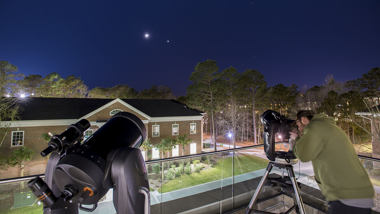 Student on top of building with two telescopes looking at night sky